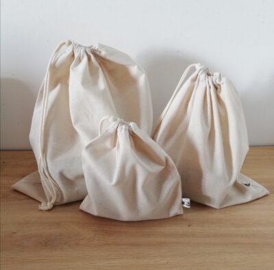 photo d'un lot de trois sacs à vrac (remplis) de tailles différentes, confectionnés dans un coton naturel beige. Les sacs à vrac se ferment à l'aide d'un cordon et d'une perle en bois