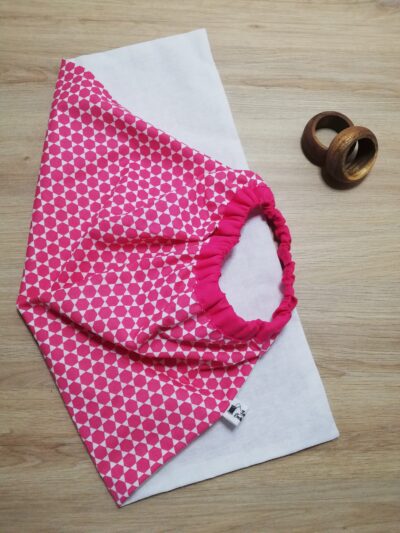 photo d'une serviette de table pour enfant, coton blanc uni d'un côté et rose avec motifs géométriques de l'autre. Un élastique en haut de la serviette permet aux enfants de pouvoir la mettre facilement autour du cou.