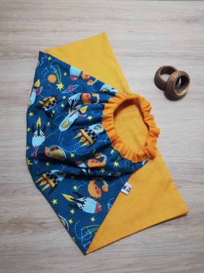 photo d'une serviette de table pour enfant, coton orange uni d'un côté et bleu avec pour motif des animaux dans l'espace. Un élastique en haut de la serviette permet aux enfants de pouvoir la mettre facilement autour du cou.