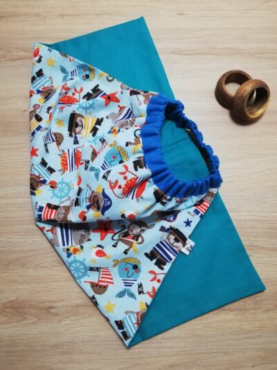 photo d'une serviette de table pour enfant, coton bleu uni d'un côté et bleu avec pour motif des animaux en marinières. Un élastique en haut de la serviette permet aux enfants de pouvoir la mettre facilement autour du cou.